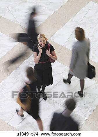 Business woman using mobile phone standing amongst people walking elevated view long exposure View Large Photo Image Picture - Business woman using mobile phone standing amongst people walking elevated view long exposure. Fotosearch