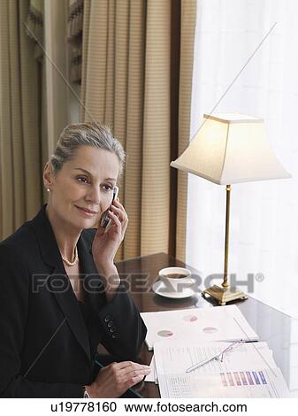 Stock Image - Business woman using mobile phone sitting at desk elevated view. Fotosearch