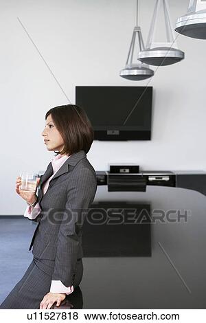 Stock Photo - Business woman with drink leaning against table in conference room. Fotosearch