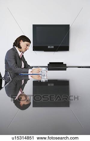 Stock Image - Business woman writing at table in conference room. Fotosearch