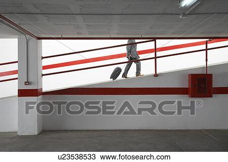 Stock Image - Businessman walking up ramp in parking garage with luggage. Fotosearch