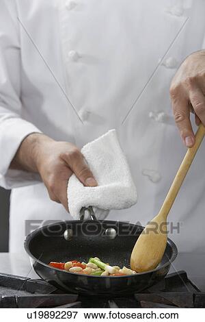 Stock Photo - Chef cooking food in frying pan mid-section. Fotosearch