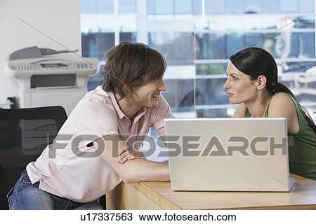 Stock Image - Colleagues using laptop at desk in office. Fotosearch