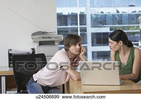 Stock Photo - Colleagues using laptop at desk in office. Fotosearch