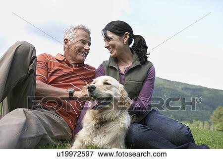 Stock Photo - Couple and golden retriever resting on grass. Fotosearch