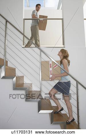 Stock Image - Couple carrying boxes upstairs in new home. Fotosearch