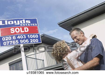 Couple embracing outside new home with sold sign View Large Photo Image Stock Photography - Couple embracing outside new home with sold sign. Fotosearch