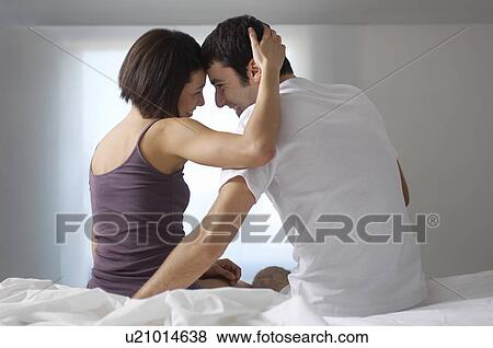 Stock Photo - Couple embracing sitting on bed back view. Fotosearch