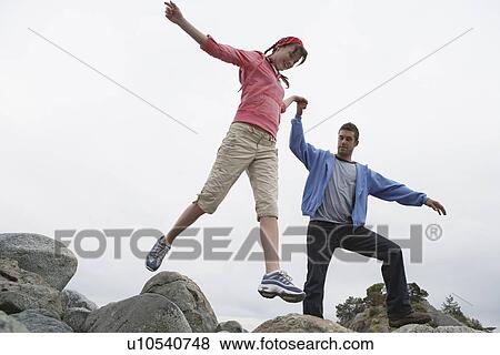 Couple holding hands jumping on rocks View Large Photo Image Stock Photo - Couple holding hands jumping on rocks. Fotosearch