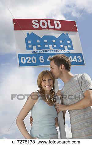 Couple holding sold sign against sky man kissing woman View Large Photo Image Stock Photo - Couple holding sold sign against sky man kissing woman. Fotosearch