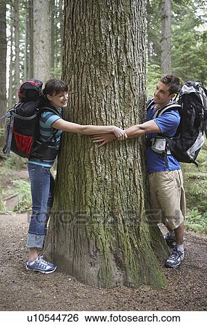 Couple hugging tree in forest View Large Photo Image Stock Photograph - Couple hugging tree in forest. Fotosearch