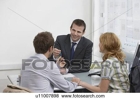 Couple in estate agents real estate agent handing man pen View Large Photo Image Stock Photo - Couple in estate agents real estate agent handing man pen. Fotosearch