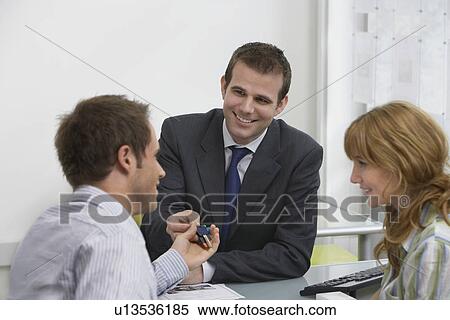 Stock Photography - Couple in estate agents real estate agent handing man pens. Fotosearch