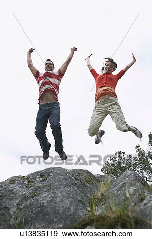 Couple leaping with arms raised over rock View Large Photo Image Stock Photo - Couple leaping with arms raised over rock. Fotosearch