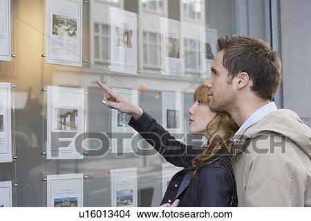 Couple looking in window outside estate agents View Large Photo Image Picture - Couple looking in window outside estate agents. Fotosearch