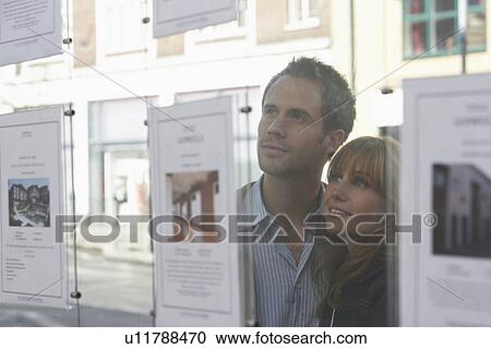 Couple looking through window at estate agents View Large Photo Image Stock Image - Couple looking through window at estate agents. Fotosearch