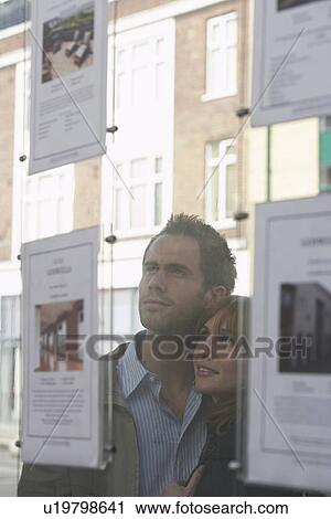 Stock Image - Couple looking through window at estate agents. Fotosearch