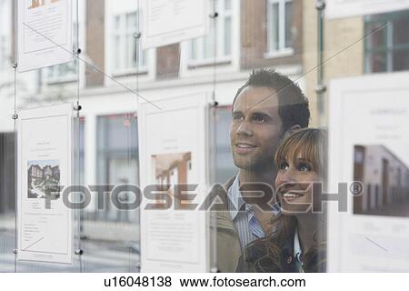 Couple looking through window at estate agents View Large Photo Image Stock Photo - Couple looking through window at estate agents. Fotosearch