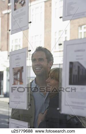 Couple looking through window at estate agents View Large Photo Image Stock Photo - Couple looking through window at estate agents. Fotosearch