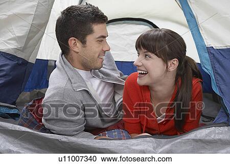Stock Image - Couple lying side by side in tent laughing. Fotosearch