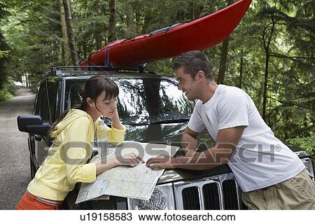 Stock Image - Couple observing map on car bonnet in forest. Fotosearch