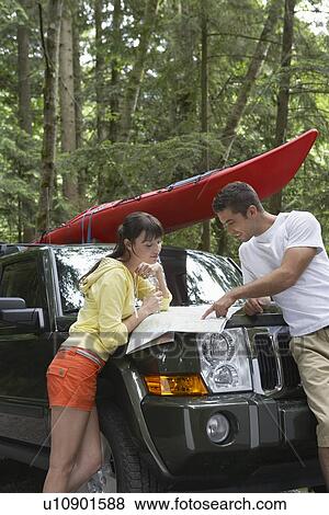 Stock Photo - Couple observing map on car bonnet in forest. Fotosearch