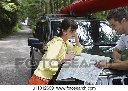 Stock Photo - Couple observing map on car bonnet in forest. Fotosearch