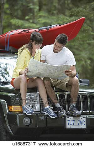 Couple observing map sitting on car View Large Photo Image Stock Photo - Couple observing map sitting on car. Fotosearch