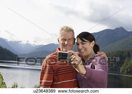 Stock Photo - Couple photographing selves mountains in background. Fotosearch