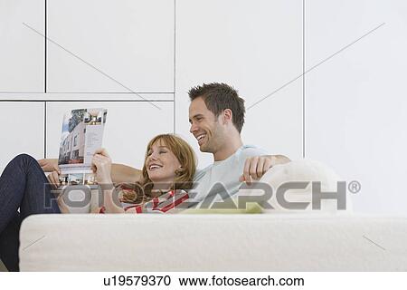 Stock Image - Couple reading brochure on sofa. Fotosearch