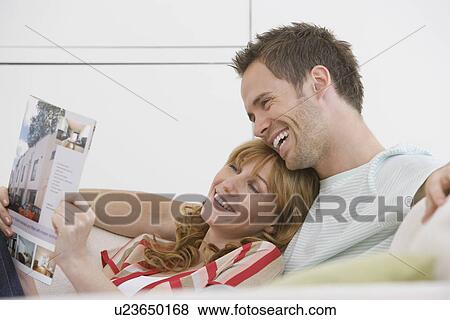 Stock Photo - Couple reading brochure on sofa. Fotosearch
