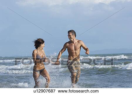 Stock Photo - Couple running in surf smiling. Fotosearch