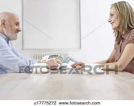 Couple sitting at table with coffee cups reading magazine together View Large Photo Image Stock Image - Couple sitting at table with coffee cups reading magazine together. Fotosearch
