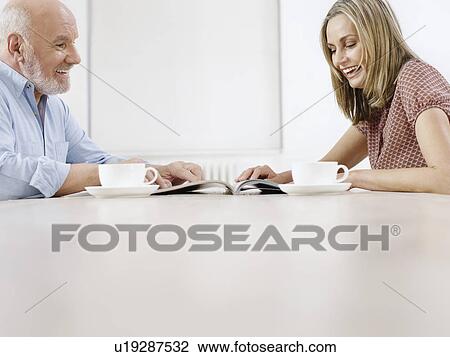 Couple sitting at table with coffee cups reading magazine together View Large Photo Image Stock Image - Couple sitting at table with coffee cups reading magazine together. Fotosearch