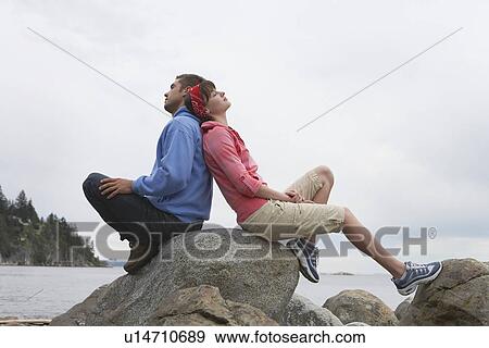 Couple sitting back to back on rocks by ocean View Large Photo Image Stock Photo - Couple sitting back to back on rocks by ocean. Fotosearch