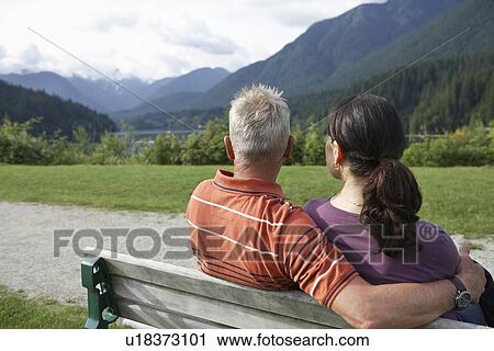 Couple sitting on bench looking at view back view View Large Photo Image Stock Image - Couple sitting on bench looking at view back view. Fotosearch