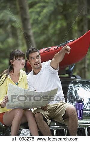 Couple sitting on car looking at map man pointing View Large Photo Image Stock Photo - Couple sitting on car looking at map man pointing. Fotosearch