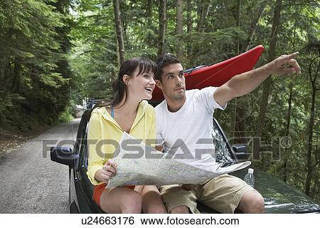 Couple sitting on car looking at map man pointing View Large Photo Image Stock Photograph - Couple sitting on car looking at map man pointing. Fotosearch