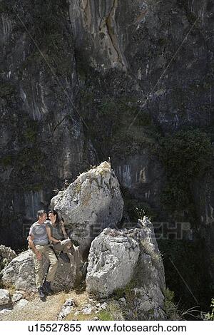 Stock Photography - Couple sitting on mountain top elevated view. Fotosearch