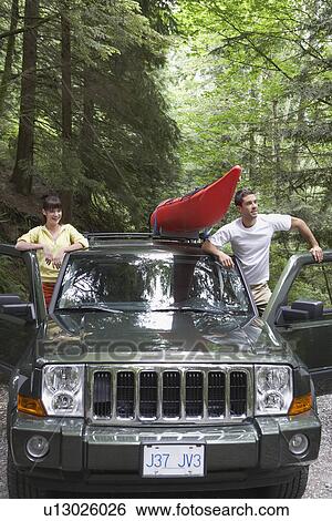 Stock Photograph - Couple standing with car in forest. Fotosearch