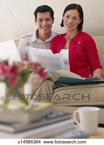 Couple using laptop and holding documents sitting on sofa portrait View Large Photo Image Picture - Couple using laptop and holding documents sitting on sofa portrait. Fotosearch