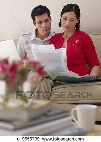 Stock Photo - Couple using laptop and holding documents sitting on sofa. Fotosearch