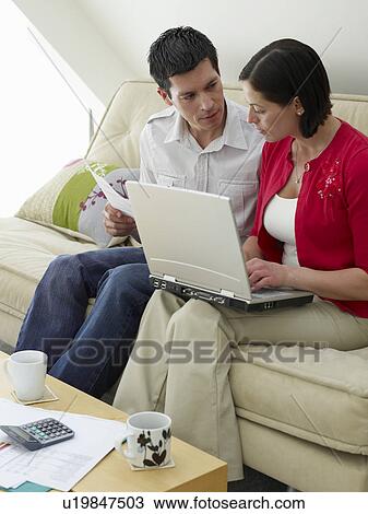 Couple using laptop sitting on sofa View Large Photo Image Stock Image - Couple using laptop sitting on sofa. Fotosearch