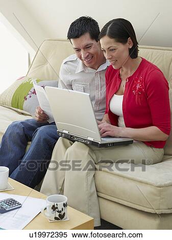 Couple using laptop sitting on sofa View Large Photo Image Stock Photography - Couple using laptop sitting on sofa. Fotosearch