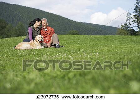 Stock Photography - Couple with golden retriever sitting in meadow. Fotosearch