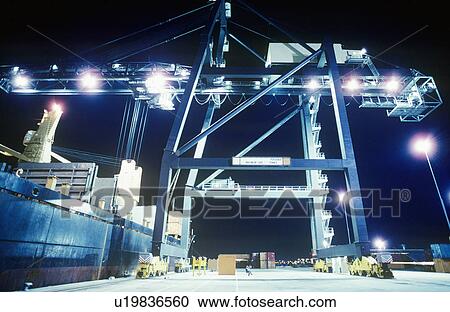 Stock Image - Crane loading container ship at night. Fotosearch