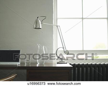 Stock Image - Desk with laptop lamp and jug of water. Fotosearch