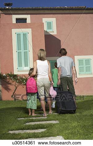 Stock Image - Family with three children (6-11) entering house with luggage back view. Fotosearch