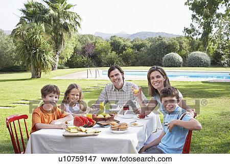 Stock Photo - Family with three children (6-11) sitting at table in garden portrait. Fotosearch