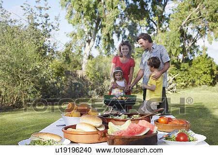 Stock Image - Family with two children (5-6) grilling table in foreground. Fotosearch